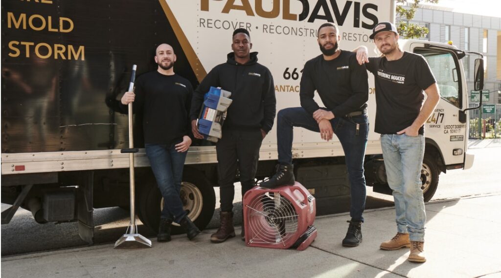 Paul Davis Restoration team members in uniform standing beside a service truck with drying equipment and tools, providing water, fire, and mold restoration services in Staten Island, NY